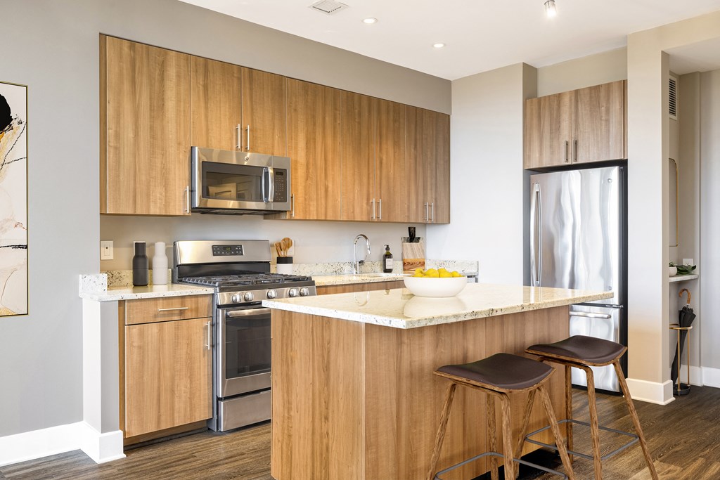 a kitchen with wooden cabinets and a counter with two stools  at The Bartlett, Arlington, VA, 22202