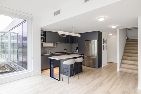 a kitchen with an island with three stools in front of it and a staircase