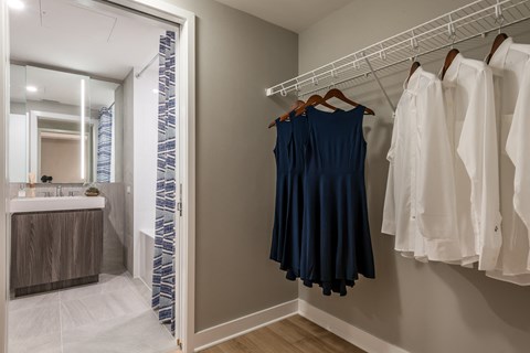 a walk in closet with clothes hanging on a rack and a bathroom with a sink