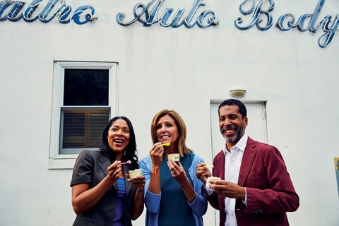 three people eating cupcakes in front of a white building