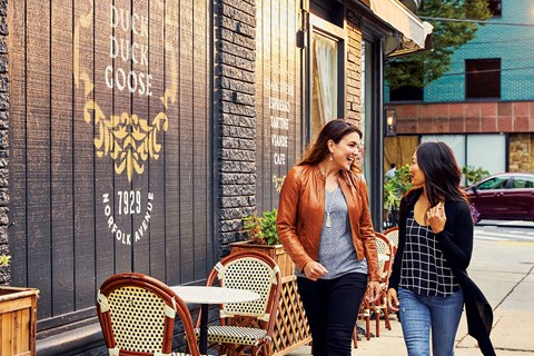 two women walking down a sidewalk outside of a restaurant