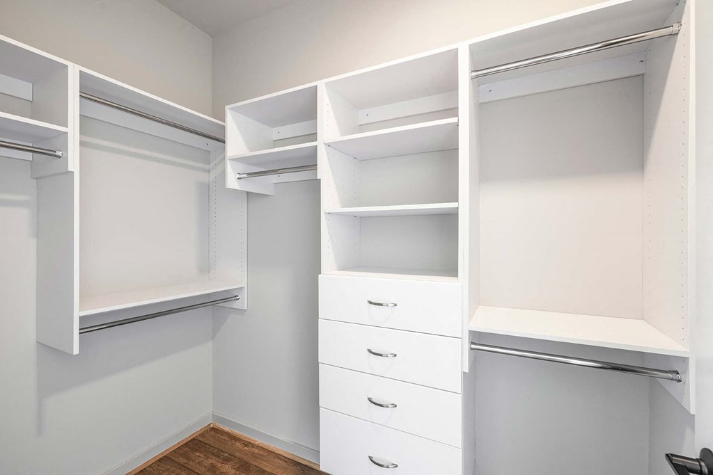 a walk in closet with white shelves and drawers