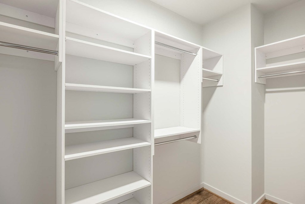 a walk in closet with white shelves and