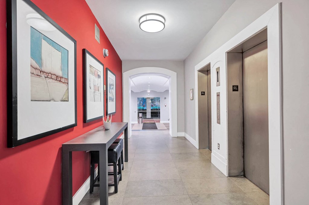 A hallway with a red wall and a bench with a table and chairs.