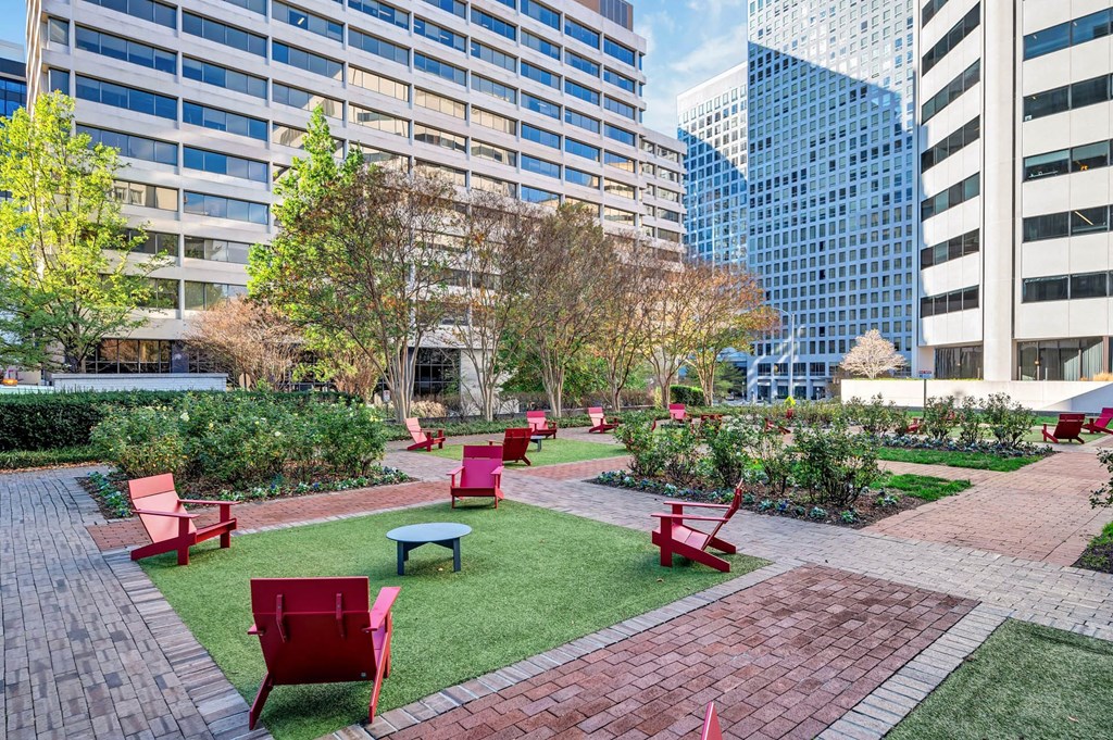 A park with red chairs and tables is surrounded by tall buildings.