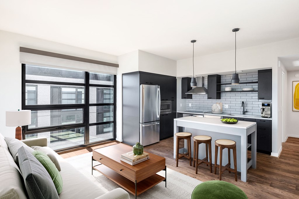 a living area with a couch coffee table a table with three stools and a kitchen with