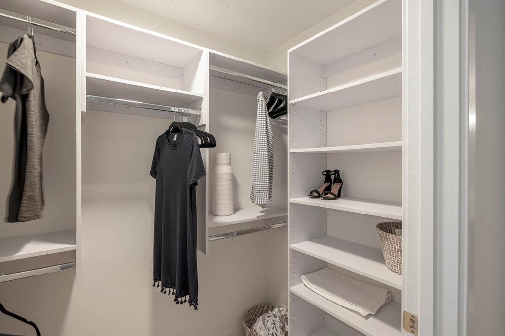a walk in closet with white shelves and clothes