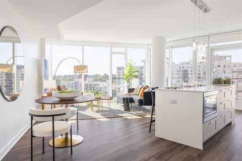 A modern kitchen with a dining table and chairs in the foreground and a view of the city through the windows.