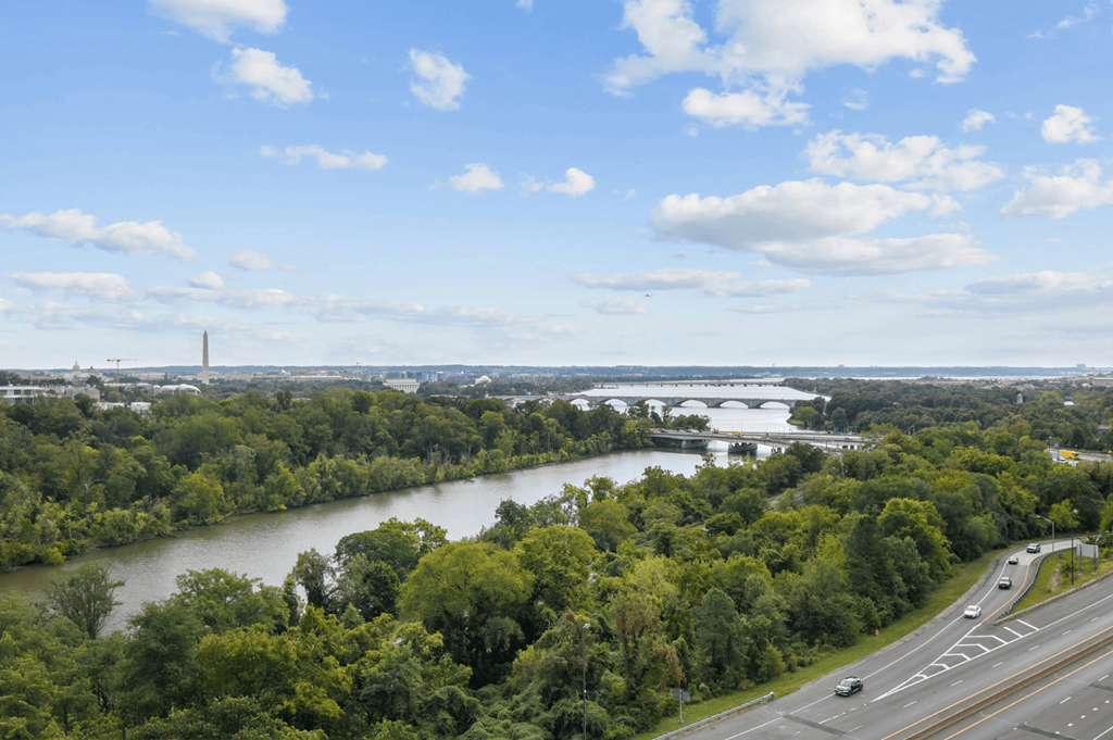 A river flows through a green forest with a highway running parallel to it.
