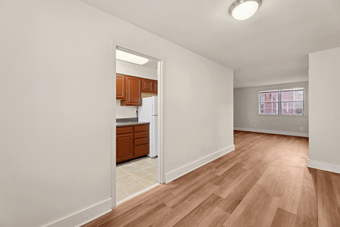 A kitchen with wooden cabinets and a refrigerator is visible through an open door.
