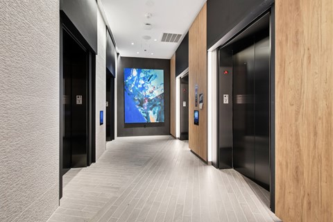 A hallway with a large screen on the wall and elevators on the side.