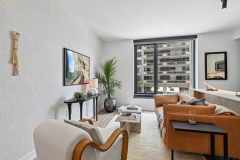 A living room with a white sofa, a brown armchair, a coffee table, and a large window with a view of a building.