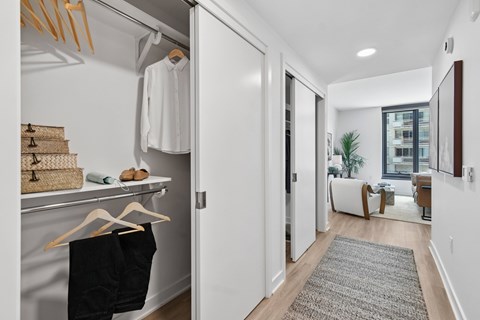 A white closet with clothes hanging and a basket on the shelf.
