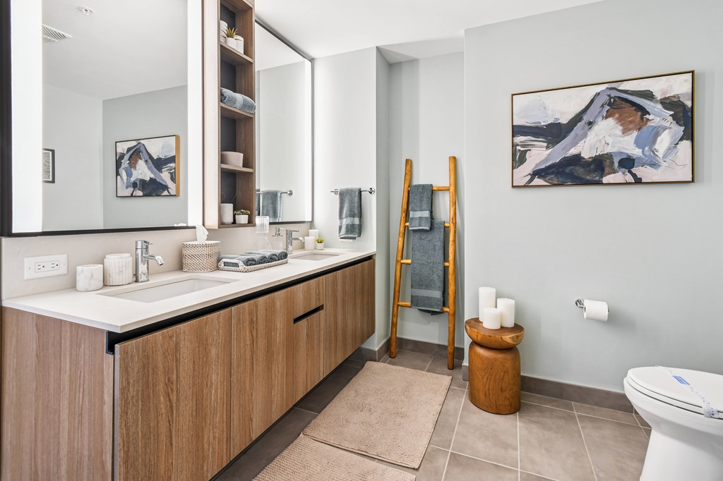 A bathroom with a white toilet, a sink with a mirror above it, and a painting on the wall.