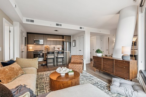A living room with a couch, a coffee table, and a kitchen area in the background.