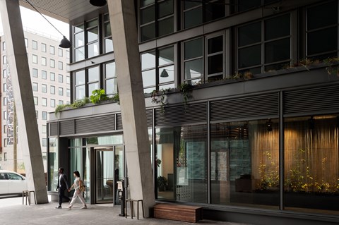 A modern building with a glass facade and a couple walking in front.