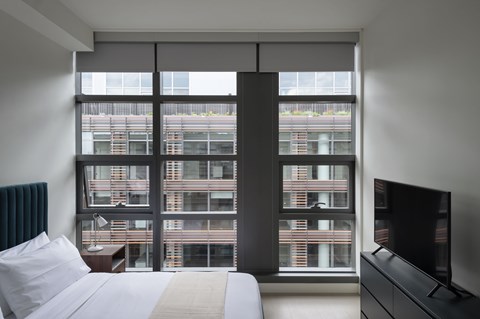 A bedroom with a large bed, a television, and a window overlooking a cityscape.