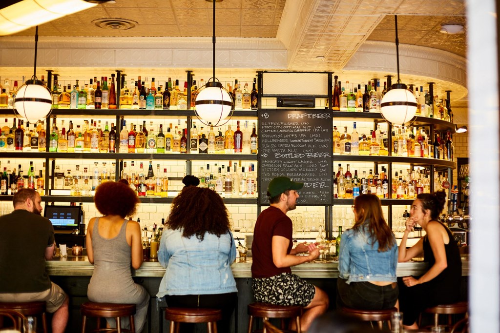 a group of people sitting at a bar in front of a bar filled with alcohol