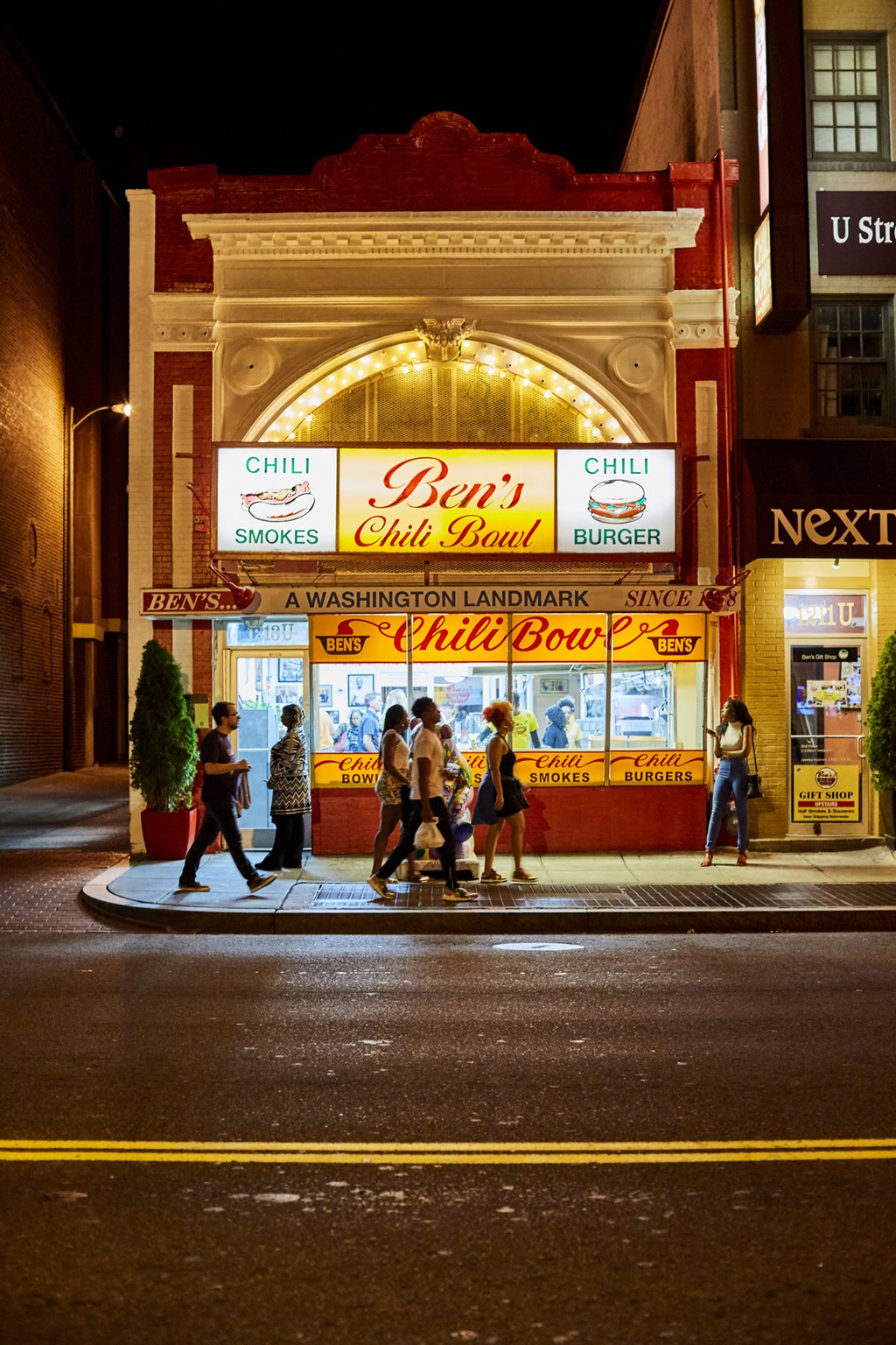 people walking in front of a restaurant on a street at night