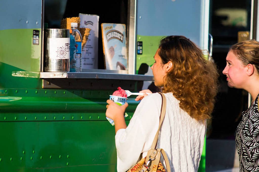 two women standing in front of a food cart eating ice cream