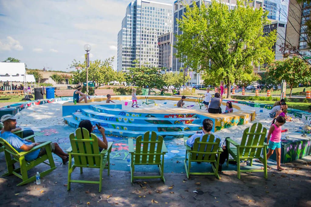 people sitting in green chairs around a pool in a park