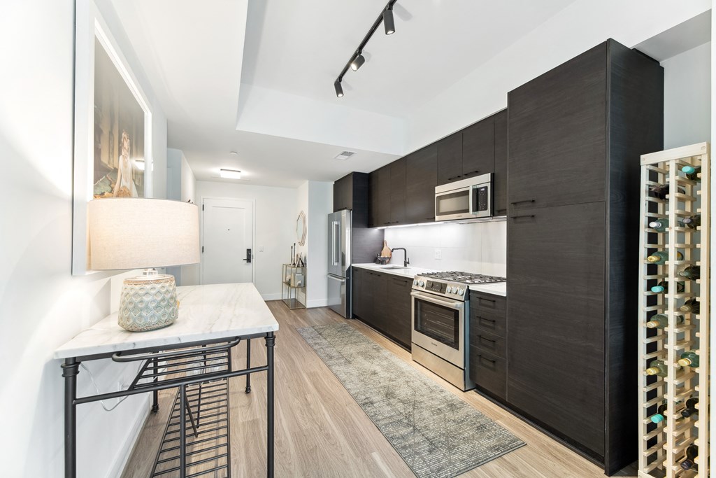 a kitchen with dark wood cabinets and white countertops and a table with a lamp