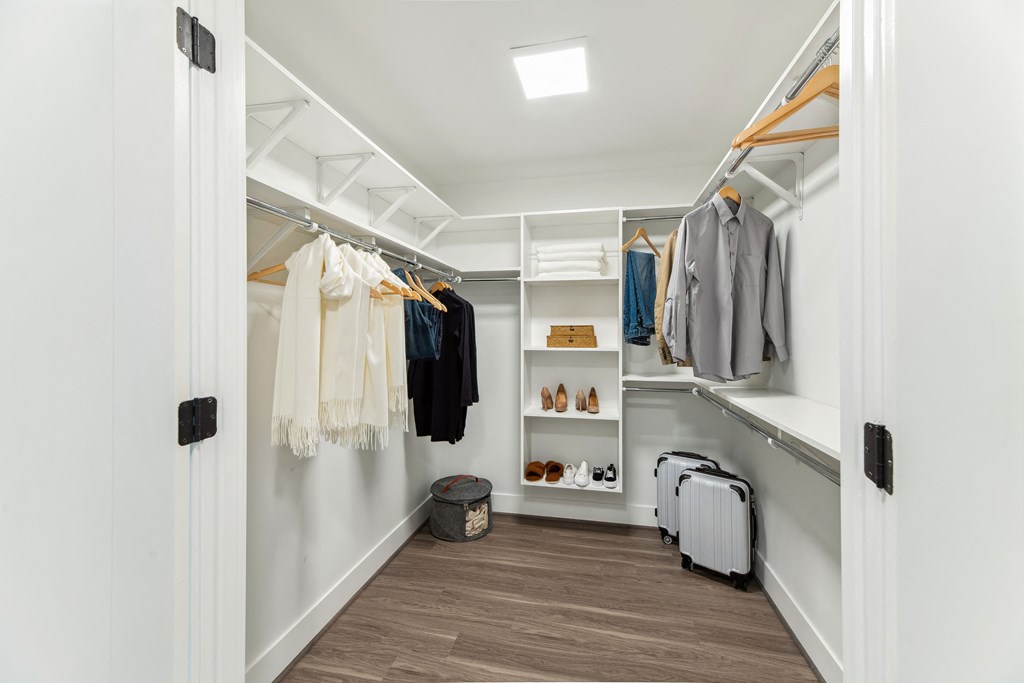 a walk in closet with white walls and wooden floors and a white closet with shelves