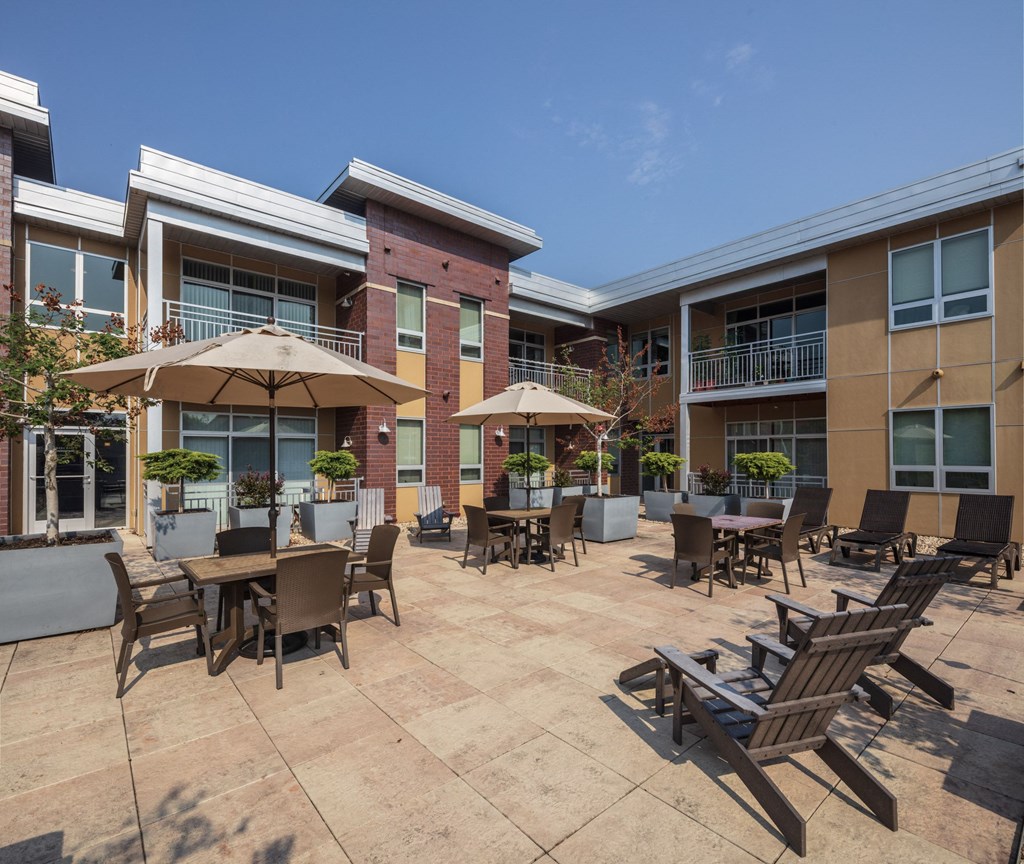 a patio with tables and chairs and umbrellas in front of an apartment building