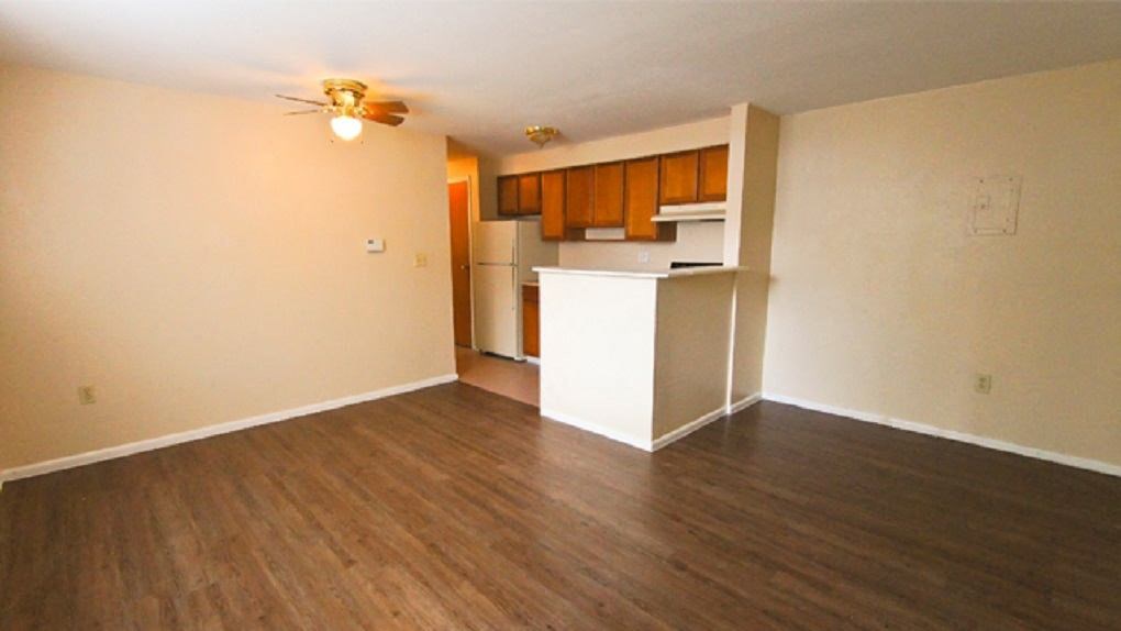 an empty living room with a kitchen and a ceiling fan