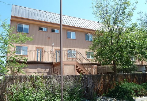 A brown house with a metal roof and a tree in front.