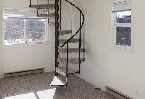A spiral staircase with a carpeted floor and a window with blinds.