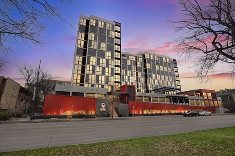 A modern building with a red and grey facade stands in front of a tree.