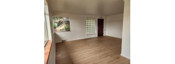 A room with wooden flooring and a window with a view of trees.
