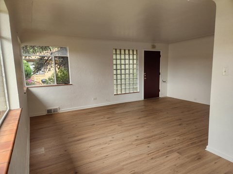 A room with wooden flooring and a window with a view of trees.