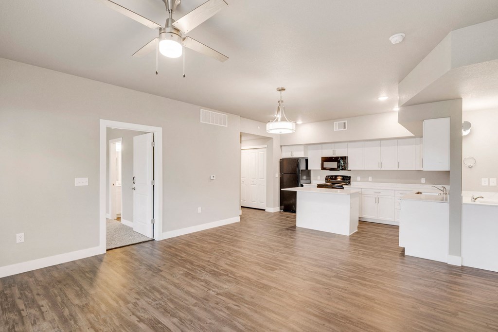 an empty living room with a kitchen and a ceiling fan