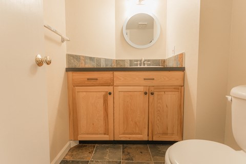 A bathroom with a toilet, a mirror, and a wooden cabinet.