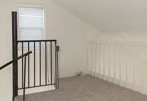 A room with a carpeted floor and a staircase with a black railing.