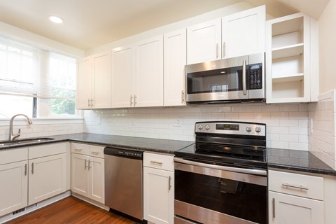 a kitchen with white cabinets and black counter tops and a stove and microwave