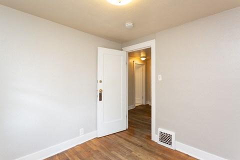 a bedroom with white walls and wood flooring and a door to a hallway