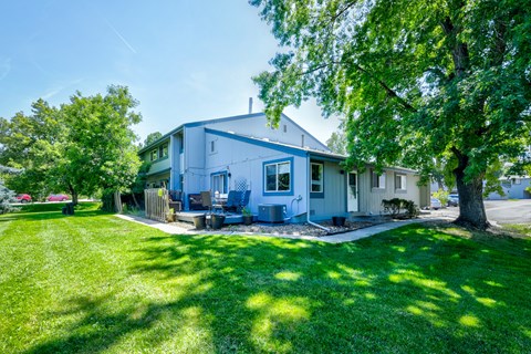 A house with a blue and white exterior is surrounded by a green lawn and trees.
