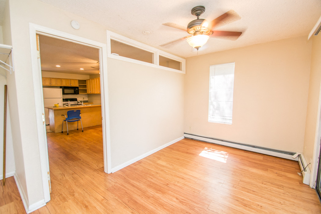 A room with a ceiling fan and a doorway leading to a kitchen.