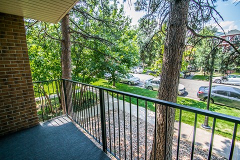 A balcony with a black railing overlooks a street with cars and trees.