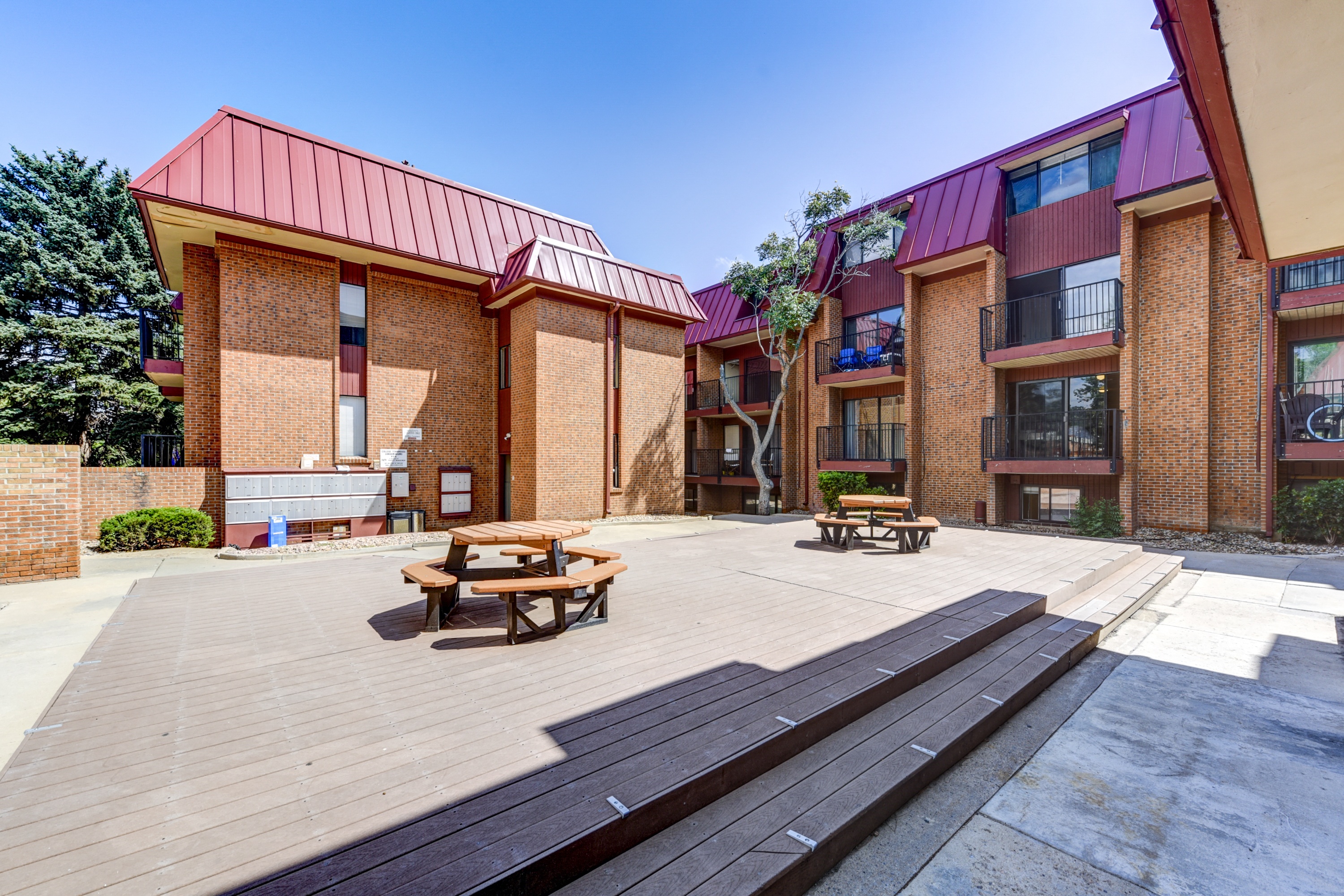 two picnic tables on a wooden deck in front of two brick buildings