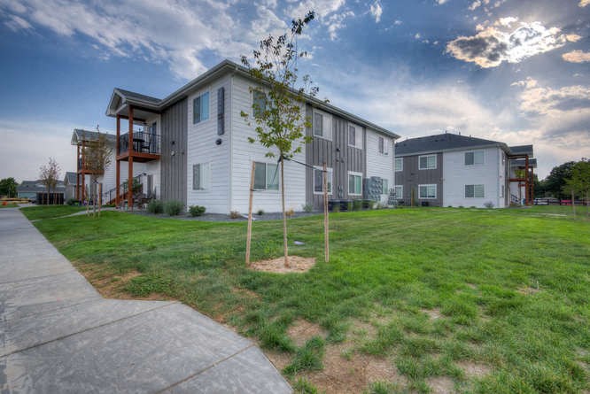 a white building with a gray roof and a green lawn