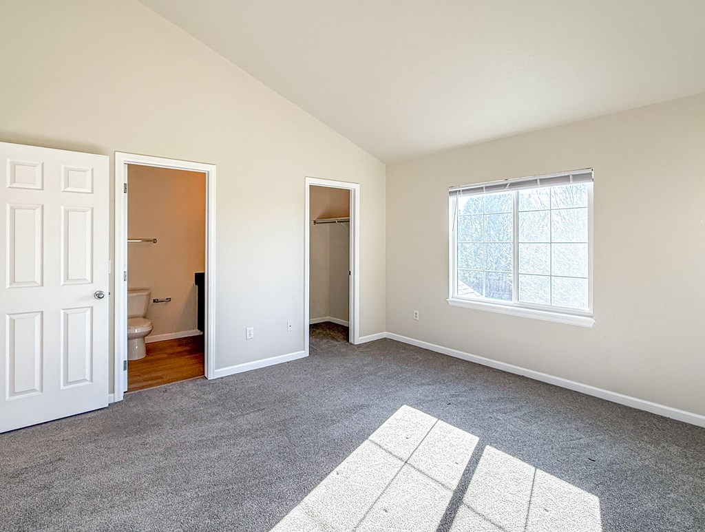 A room with a white door, a window, and a carpeted floor.