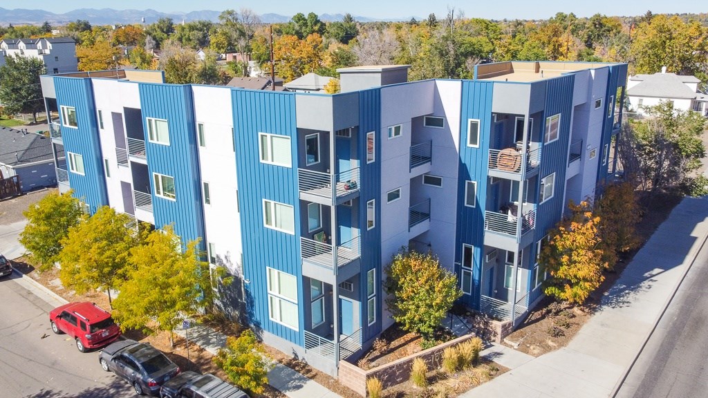 A blue and white apartment building with a red car parked in front.