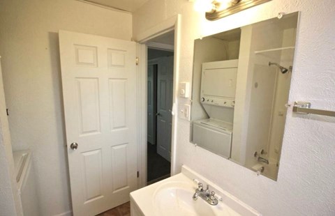 A white bathroom with a sink, mirror, and a door.
