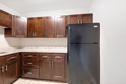 A black refrigerator stands in a kitchen with brown cabinets.