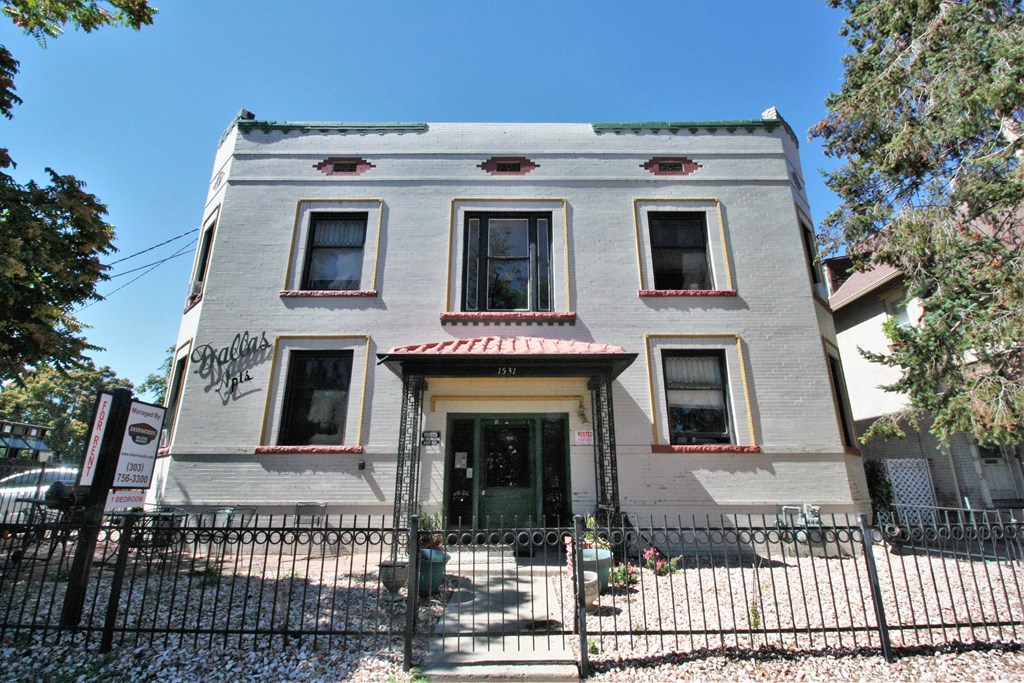 A grey two-story house with a red awning and a black fence in front.