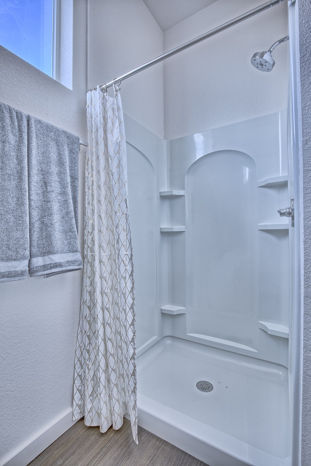 A white bathroom with a shower and a towel hanging on the wall.
